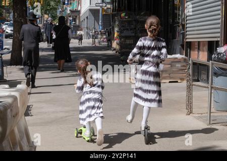 Due sorelle con code di pony vestite in modo identico cavalcano i loro scooter su Lee Avenue a Williamsburg, Brooklyn, New York, un quartiere ebraico chassidico. Foto Stock