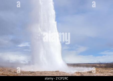 I turisti si meravigliano di fronte all'eruzione del geyser Strokkur, che invia un pennacchio di vapore e acqua in alto nell'aria. Questa meraviglia geotermica è un'attrazione popolare Foto Stock