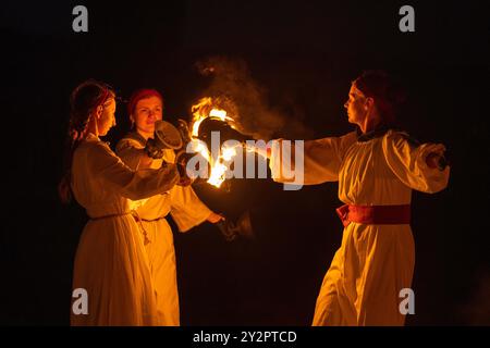 REGIONE DI TVER, RUSSIA - 21 LUGLIO 2023: Tre ragazze in abiti antichi illuminano un fuoco in una notte buia. Festival storico "Epic Coast-2023" Foto Stock