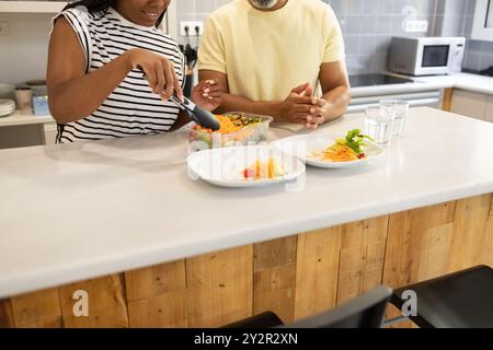 Una donna afroamericana e un uomo indiano che si uniscono alla preparazione dei pasti in un ambiente moderno della cucina Foto Stock