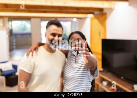 Una coppia gioiosa si trova nella loro nuova casa la donna, afroamericana nera, tiene le chiavi della loro nuova casa, sorridendo e puntando verso il cameriere Foto Stock