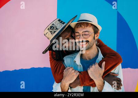 Un uomo afroamericano e il suo partner caucasico condividono un caldo abbraccio e un bacio sulla guancia, su uno sfondo urbano colorato, che ritrae affetto e Foto Stock