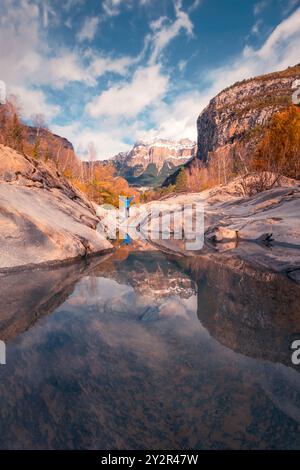 Una tranquilla scena autunnale nel Parco Nazionale di Ordesa, con una persona in piedi su rocce lisce accanto alle acque riflettenti del fiume Ara, circondato da Foto Stock