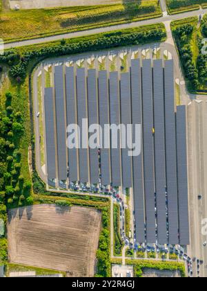 Dall'alto, questa vista con drone mette in evidenza un vasto parco solare accanto a parcheggi ben organizzati. Le diverse sfumature di blu dai pannelli solari c Foto Stock