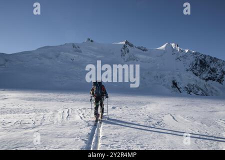 Vista posteriore di un alpinista irriconoscibile con zaino che sale su un sentiero innevato nelle tranquille Alpi svizzere vicino a Zermatt. Foto Stock