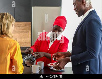 Tre professionisti si impegnano durante una rilassante pausa caffè. La donna in rosso serve il caffè, sorridendo il suo collega che sta guardando anche lui Foto Stock