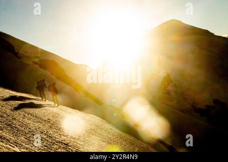 Vista posteriore di alpinisti irriconoscibili con attrezzatura da trekking che sale su un ripido sentiero illuminato dal sole nelle Alpi svizzere vicino a Zermatt. Oggetti polvere e luce solare brillante Foto Stock