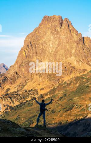 Vista posteriore di un uomo irriconoscibile che festeggia in un'escursione, ammirando il maestoso PIC du Midi d'Ossau nei Pirenei francesi. Foto Stock