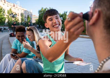 Un gruppo di amici LGBTQIA+ che condividono un momento di gioia all'aperto. Una persona applica scherzosamente il trucco al volto di un amico, mentre altre si impegnano in conversazione Foto Stock