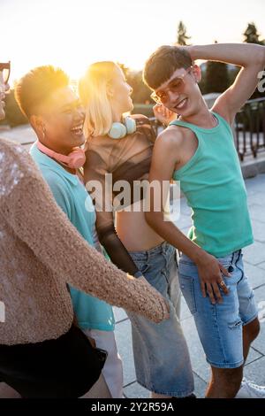 Un gruppo gioioso di amici LGBTQIA+ condivide risate e abbraccia mentre si godono uno sfondo al tramonto, celebrando la diversità e l'amicizia. Foto Stock