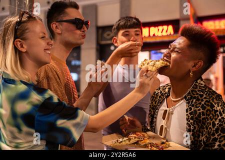 Gli allegri amici LGBTQIA+ si godranno un momento di pizza informale insieme, mostrando diversità e comunità in un vivace ambiente urbano. Foto Stock