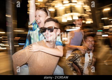 Un vivace gruppo di amici LGBTQIA+ che ridono e si divertono durante una serata fuori, catturati in un movimento dinamico e sfocato, a simboleggiare l'energia e il movimento Foto Stock