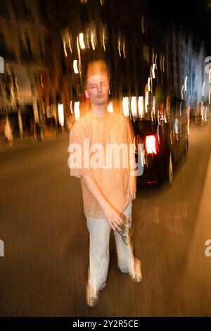 Una persona non binaria posa tra calde e dinamiche strisce di luce, creando un effetto astratto e sfocato dal movimento. Foto Stock