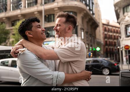 Un'immagine commovente di una giovane coppia gay multietnica che si abbraccia con gioia in una strada trafficata della città, condividendo un momento di risate e vicinanza, con l'urba Foto Stock
