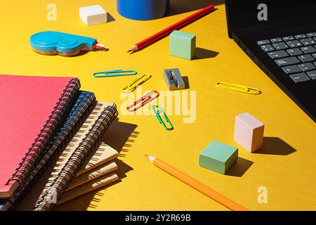 Vivaci forniture scolastiche sparse su una superficie gialla, con notebook, matite, gomme e un notebook, simbolizzazione della preparazione e dell'organizzazione f Foto Stock