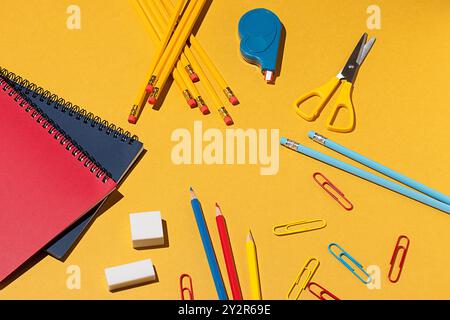 Vista dall'alto di un assortimento di materiale scolastico su un vivace sfondo giallo. Questa immagine presenta matite colorate, notebook, forbici, gomme e p Foto Stock
