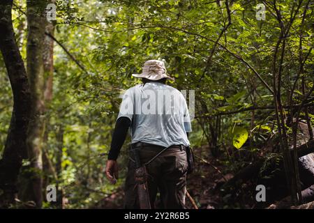 Un uomo con un cappello da secchio vaga attraverso la lussureggiante e verde foresta pluviale della Costa Rica, mostrando la bellezza naturale e il fitto fogliame della regione Foto Stock