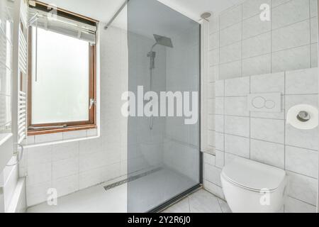 Un bagno elegante e moderno con box doccia in vetro, piastrelle in marmo bianco e una finestra che fornisce illuminazione naturale. Foto Stock