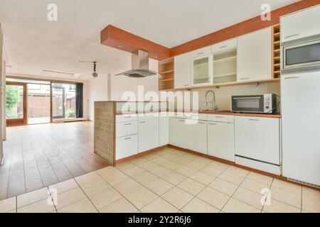 Cucina spaziosa e moderna con mobili bianchi puliti, pavimenti piastrellati e vista del giardino attraverso porte scorrevoli. Foto Stock