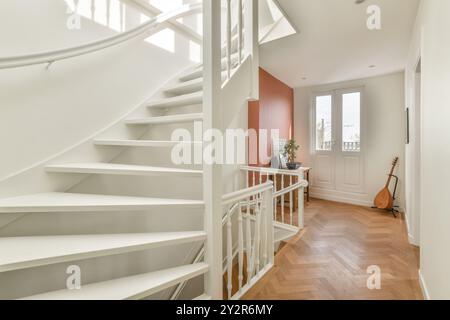 Un corridoio ben illuminato presenta una scala a spirale bianca, pavimenti in legno e un delicato tocco di colore. Foto Stock