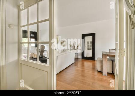 Una vista dal corridoio attraverso una porta aperta con pannelli di vetro su un luminoso soggiorno con decor elegante e arredi moderni. Foto Stock