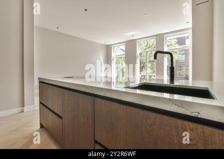 Una cucina dal design moderno ed elegante con mobili in legno con finiture lisce e un piano di lavoro in marmo bianco con lavandino integrato e rubinetto moderno. Foto Stock