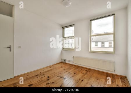 Una sala non occupata con pavimento in legno lucido, pareti bianche e due finestre che lasciano entrare luce naturale. Foto Stock