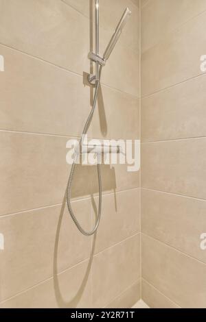 Soffione doccia elegante e moderno con tubo flessibile installato su piastrelle beige chiare in un angolo bagno contemporaneo. Foto Stock