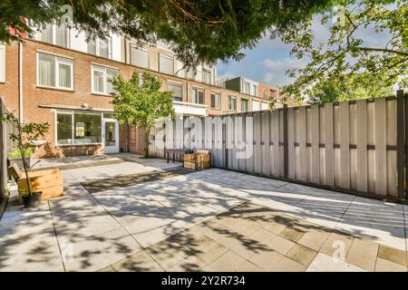 Una tranquilla casa in mattoni di periferia caratterizzata da un grande cortile piastrellato con una recinzione di legno sotto un cielo azzurro. Foto Stock