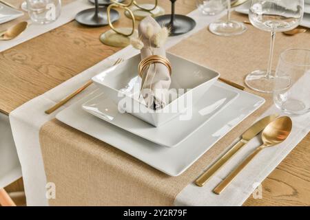 Un sofisticato tavolo da pranzo con piatti bianchi croccanti, posate d'oro e delicate decorazioni che creano un'atmosfera calda e invitante. Foto Stock