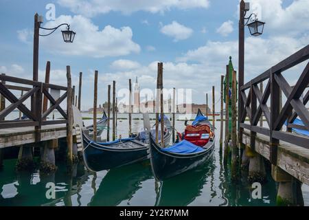 Una vista serena delle tradizionali gondole legate ai moli di legno intemprati nel cuore di Venezia, Italia, con l'iconica silhouette di San Giorgio maggiore Foto Stock