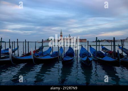 Una tranquilla vista delle gondole ricoperte di blu attraccate sulle scintillanti acque di Venezia, Italia, con l'iconica Chiesa di San Giorgio maggiore nel dorso Foto Stock