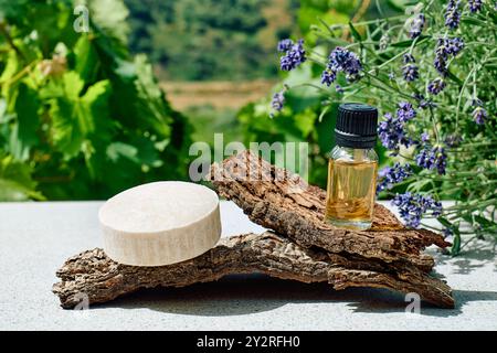 Bottiglia con olio di lavanda naturale essenziale e sapone di lavanda fatto in casa su corteccia di legno come podio per la presentazione del prodotto. Aromaterapia, alternati Foto Stock
