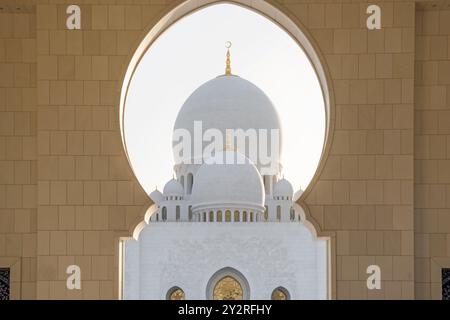 Vista delle Domes della grande Moschea dello sceicco Zayed ad Abu Dhabi, negli Emirati Arabi Uniti incorniciata da un arco ornato. Arte e architettura islamica. Popolare luogo di culto arabo e. Foto Stock