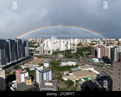 Una vista panoramica di un paesaggio urbano con un vibrante arcobaleno che si innalza su alti edifici e un mix di aree residenziali e commerciali. Foto Stock