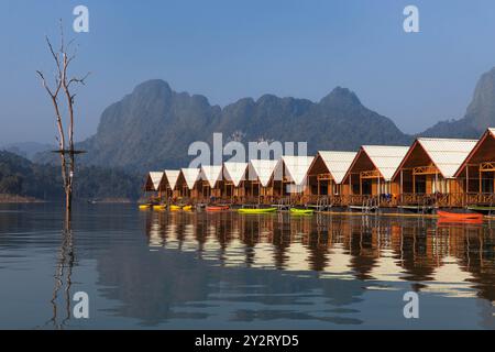 Le cabine in legno si trovano su acque tranquille, riflettendo le montagne e gli alberi circostanti. I kayak sono allineati lungo la riva, invitando a esplorare questo s Foto Stock