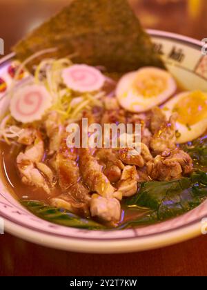 Primo piano di una deliziosa ciotola di ramen con pollo a fette, uova sode, alghe e narutomaki in un ricco brodo. Foto Stock