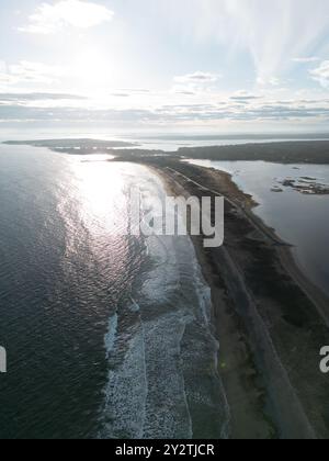 Vista aerea di un paesaggio costiero con una spiaggia sabbiosa, onde e un cielo limpido all'alba. Foto Stock