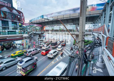 Infinite linee di veicoli, striature di movimento sfocate, corsa verso e fuori, sotto un passaggio pedonale, e linea ferroviaria sopraelevata in cemento sopraelevato Skytrain, passante Foto Stock