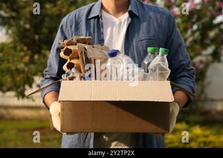 Riciclaggio. Uomo che tiene una scatola di cartone con diversi rifiuti all'aperto, primo piano Foto Stock