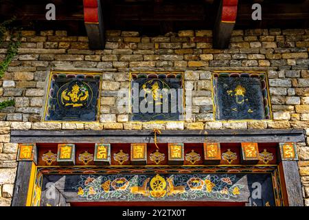 Una vista dettagliata dell'arte e dell'architettura tradizionali bhutanesi su un muro di pietra con dipinti e intagli colorati. Foto Stock