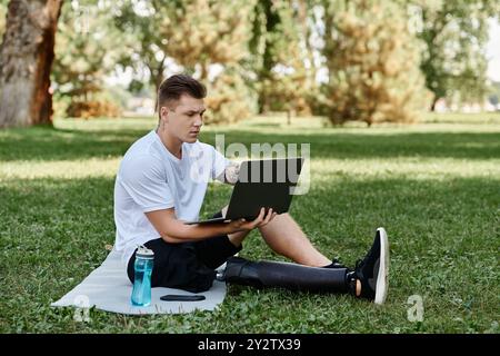 Giovane tatuato con una gamba artificiale che usa un laptop nel parco, nomade digitale Foto Stock