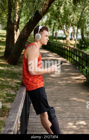 Un giovane con protesi alle gambe che usa lo smartphone, circondato dal verde del parco. Foto Stock