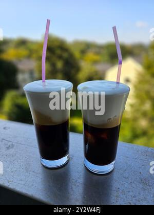 Un primo piano di due bicchieri di caffè con panna e cannucce rosa su un balcone con sfondo sfocato Foto Stock