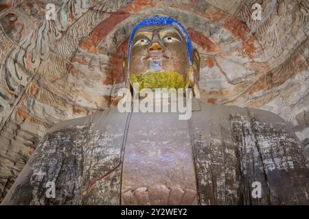 Primo piano di una grande statua di Buddha antica in una grotta con dettagli colorati alle Grotte di Yungang, Cina Foto Stock