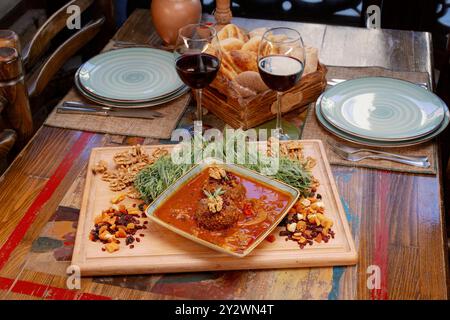 Un ambiente rustico che propone un delizioso pasto a base di polpette in salsa, noci, frutta secca e due bicchieri di vino rosso su un tavolo di legno. Foto Stock