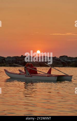Una barca bagnino che galleggia sulle acque calme al tramonto con una costa rocciosa sullo sfondo. Foto Stock