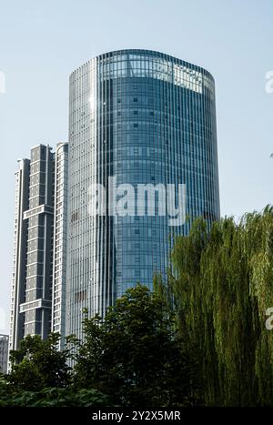 Alti e moderni edifici con facciate in vetro e vegetazione in primo piano sotto un cielo azzurro. Foto Stock