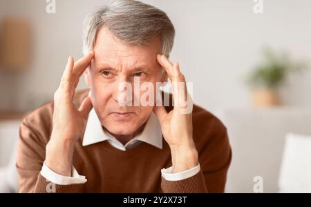 Uomo anziano con mal di testa che tocca i templi seduti sul divano Foto Stock