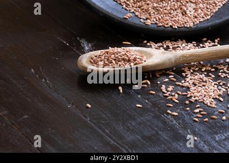 Riso rosso che cade da una ciotola e viene sparso sul tavolo accanto a un cucchiaio di legno. Foto Stock